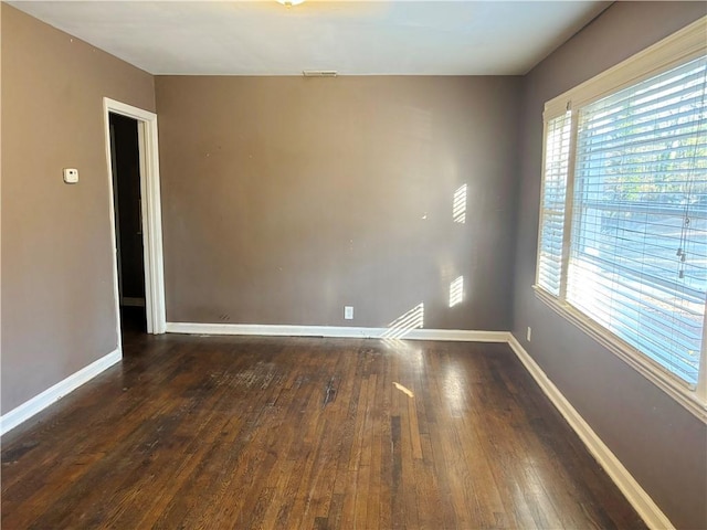 empty room featuring wood-type flooring, visible vents, and baseboards