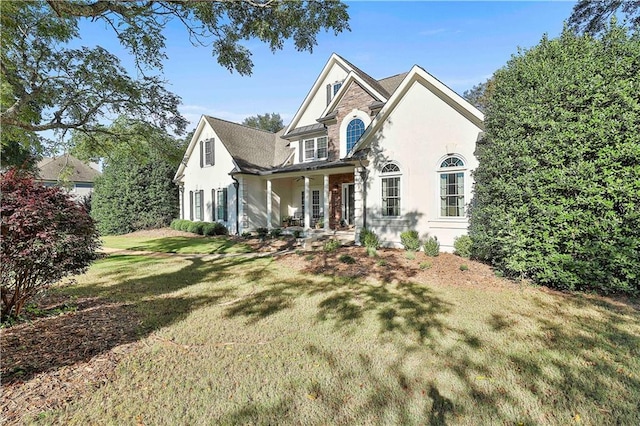 view of front of home with stucco siding, a porch, a front lawn, and stone siding
