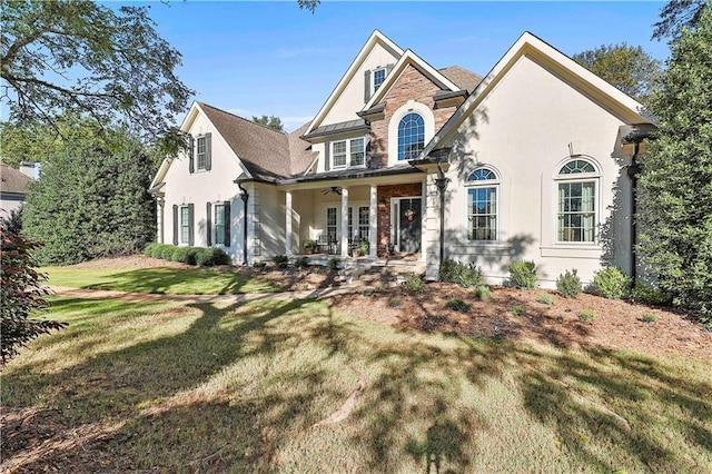 traditional home with stucco siding, a front yard, stone siding, and ceiling fan