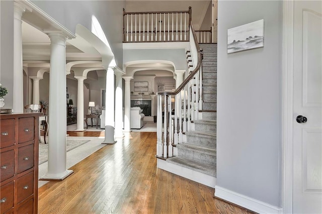 entrance foyer featuring ornate columns, wood finished floors, stairway, arched walkways, and a towering ceiling
