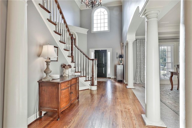 entrance foyer featuring decorative columns, wood finished floors, ornamental molding, stairs, and a towering ceiling