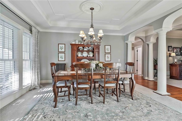 dining space with decorative columns, arched walkways, a tray ceiling, a chandelier, and ornamental molding
