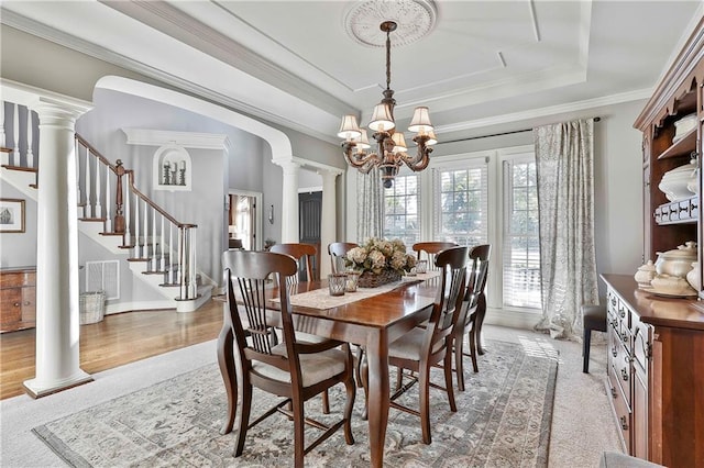 dining area featuring a chandelier, stairway, a tray ceiling, decorative columns, and light colored carpet