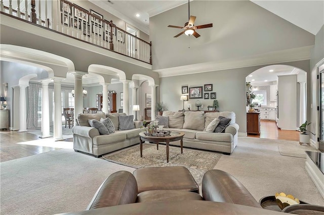 living room featuring decorative columns, a high ceiling, a ceiling fan, crown molding, and arched walkways