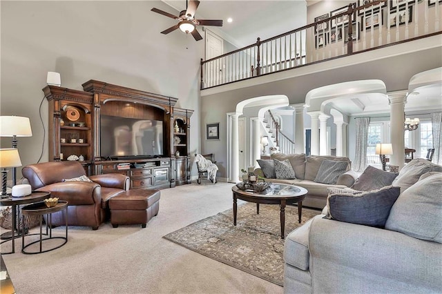 carpeted living room with decorative columns, ceiling fan, a towering ceiling, arched walkways, and stairs