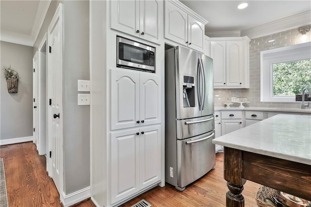 kitchen featuring stainless steel appliances, ornamental molding, a sink, white cabinetry, and light wood-style floors