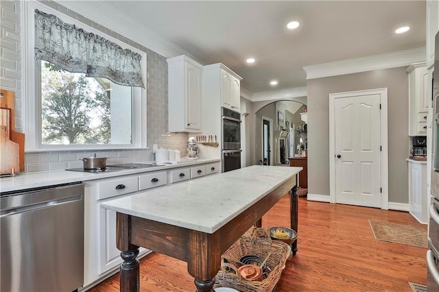 kitchen with appliances with stainless steel finishes, arched walkways, white cabinets, tasteful backsplash, and ornamental molding