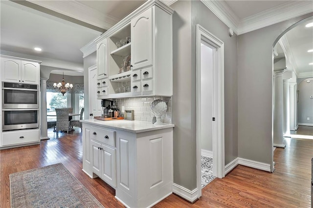 kitchen with open shelves, double oven, arched walkways, ornamental molding, and dark wood-type flooring