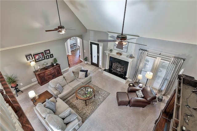carpeted living room with a ceiling fan, high vaulted ceiling, baseboards, arched walkways, and a fireplace with raised hearth