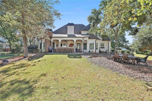 rear view of property featuring ceiling fan, a yard, stucco siding, a chimney, and covered porch