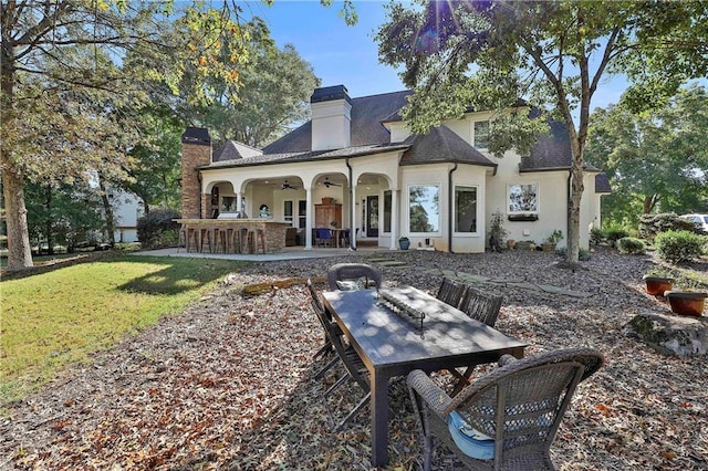 back of property with a chimney, a patio, stucco siding, a ceiling fan, and outdoor dining space