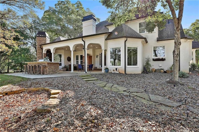 back of property with a chimney, a patio area, stucco siding, and roof with shingles