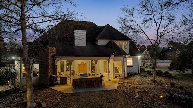 back of house at dusk featuring a patio and roof with shingles