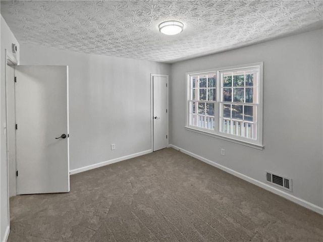 empty room featuring dark carpet and a textured ceiling