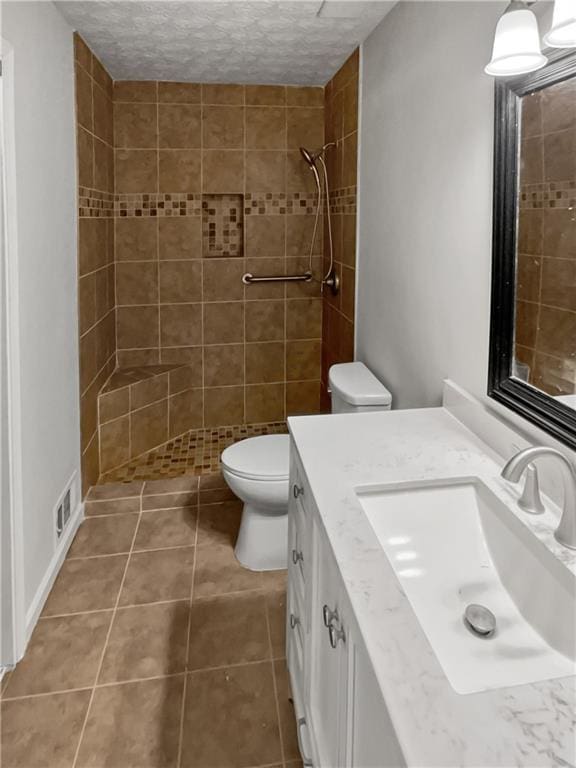 bathroom with vanity, tiled shower, toilet, tile patterned floors, and a textured ceiling