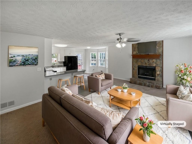 living room with light colored carpet, a stone fireplace, and a textured ceiling