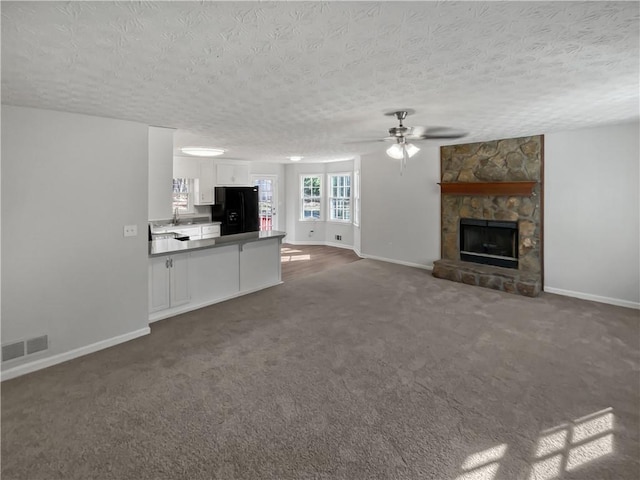 unfurnished living room with sink, ceiling fan, dark colored carpet, a textured ceiling, and a stone fireplace