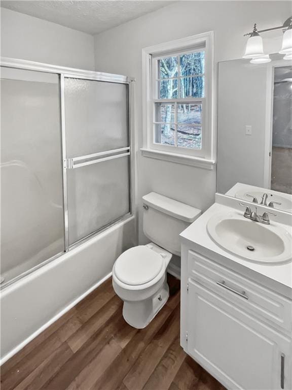 full bathroom with enclosed tub / shower combo, hardwood / wood-style floors, vanity, a textured ceiling, and toilet