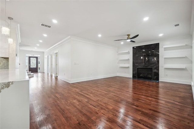 unfurnished living room with dark hardwood / wood-style floors, built in features, a fireplace, ceiling fan, and crown molding