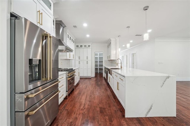 kitchen with pendant lighting, wall chimney range hood, appliances with stainless steel finishes, tasteful backsplash, and white cabinets