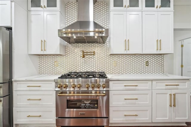 kitchen with white cabinetry, stainless steel appliances, light stone counters, decorative backsplash, and wall chimney exhaust hood