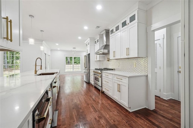 kitchen with high end appliances, white cabinets, decorative light fixtures, and wall chimney exhaust hood