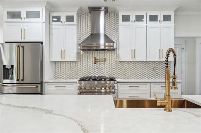 kitchen featuring tasteful backsplash, white cabinetry, premium appliances, light stone countertops, and wall chimney range hood