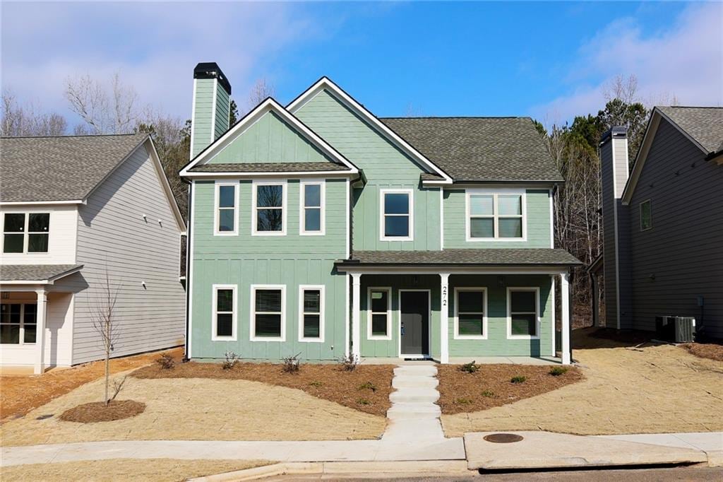 view of front of house featuring board and batten siding, a chimney, roof with shingles, covered porch, and central AC