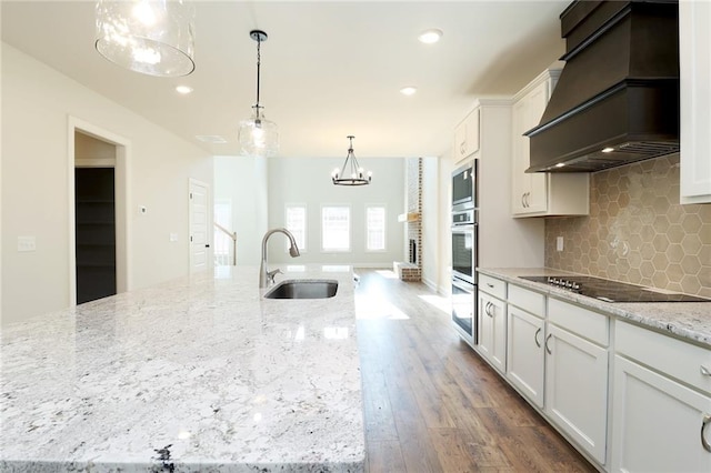 kitchen with black electric cooktop, a sink, white cabinets, tasteful backsplash, and custom range hood