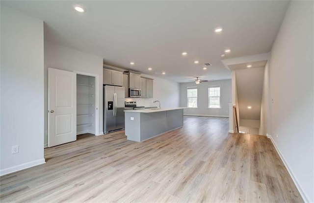 kitchen featuring gray cabinetry, an island with sink, open floor plan, appliances with stainless steel finishes, and light countertops