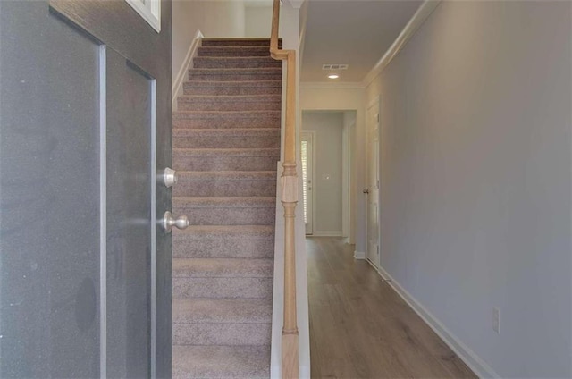 staircase with wood finished floors, baseboards, visible vents, and ornamental molding