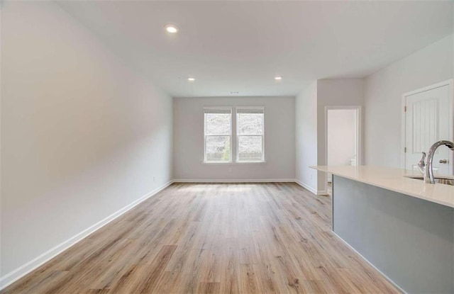 unfurnished living room featuring recessed lighting, baseboards, light wood-style floors, and a sink