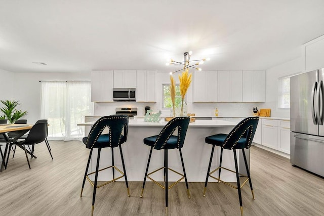 kitchen with a breakfast bar, stainless steel appliances, a notable chandelier, a center island, and white cabinetry