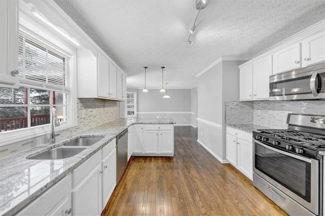 kitchen featuring kitchen peninsula, appliances with stainless steel finishes, sink, pendant lighting, and white cabinetry