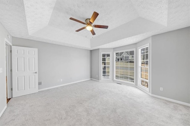 spare room featuring a textured ceiling, carpet floors, a raised ceiling, and ceiling fan