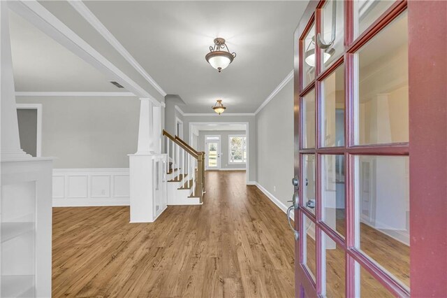 entryway with light wood-type flooring, decorative columns, and crown molding