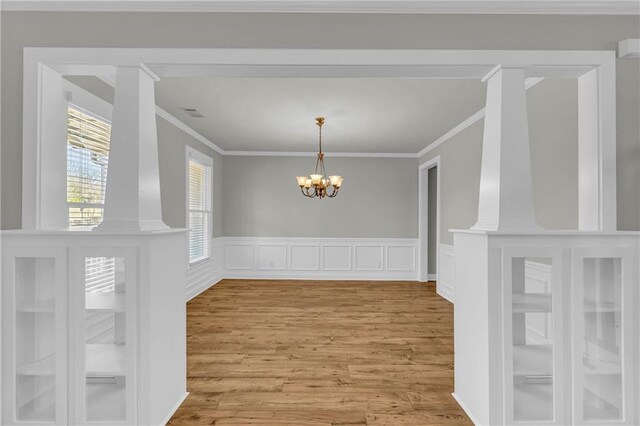 unfurnished dining area featuring ornate columns, crown molding, light hardwood / wood-style flooring, and a chandelier