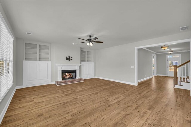 unfurnished living room with built in shelves, ceiling fan, and light wood-type flooring