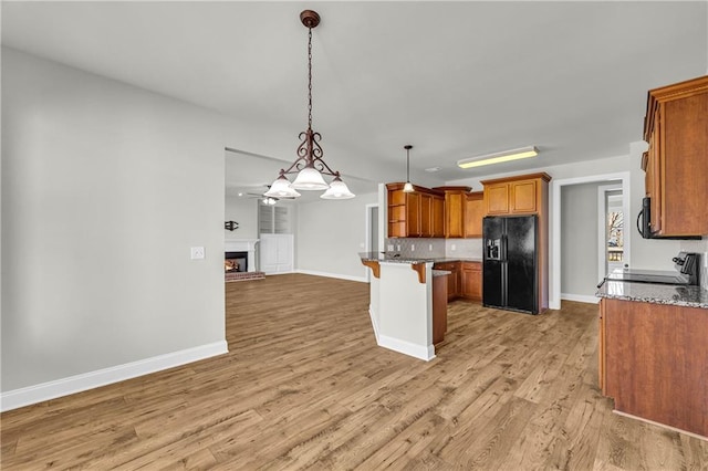 kitchen featuring a kitchen breakfast bar, tasteful backsplash, light hardwood / wood-style floors, decorative light fixtures, and black appliances