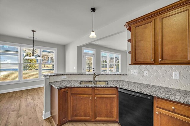 kitchen with light stone countertops, light wood-type flooring, sink, decorative light fixtures, and black dishwasher
