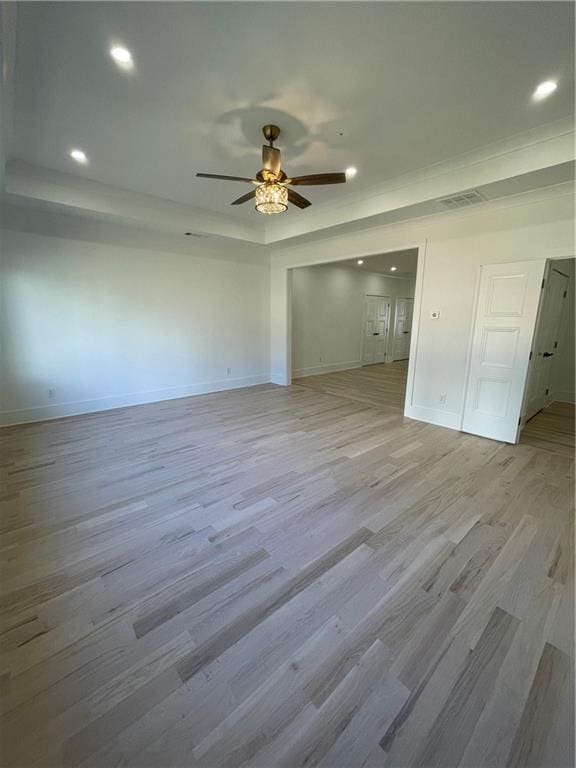 spare room featuring ceiling fan, light wood-type flooring, and a tray ceiling