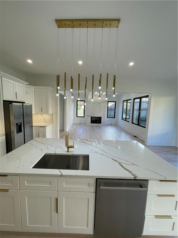 kitchen with light stone countertops, a fireplace, stainless steel appliances, light hardwood / wood-style flooring, and white cabinets