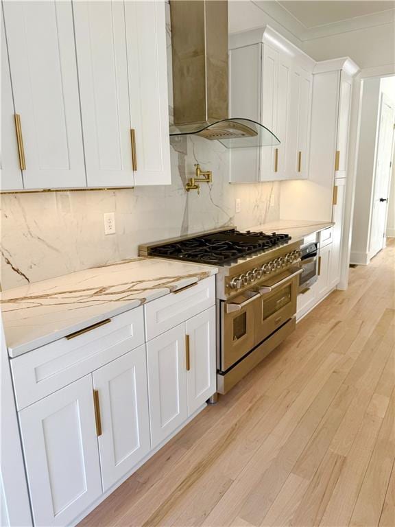 kitchen featuring appliances with stainless steel finishes, wall chimney exhaust hood, light wood-type flooring, and white cabinets