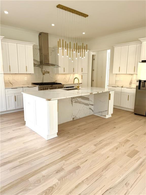 kitchen featuring stainless steel fridge, white cabinetry, a spacious island, decorative light fixtures, and wall chimney exhaust hood