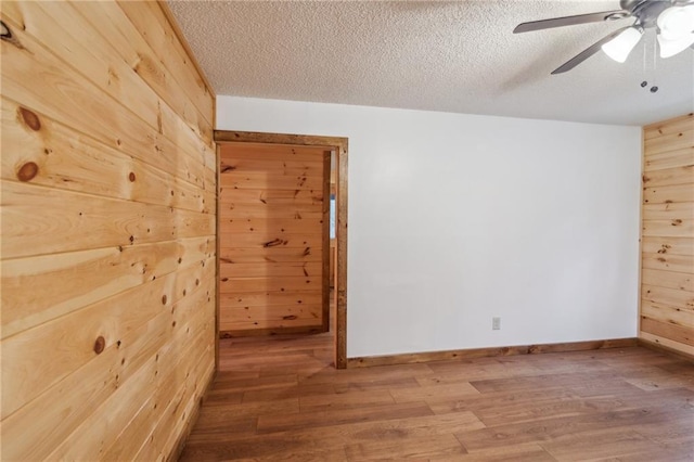 spare room with a ceiling fan, wood walls, a textured ceiling, wood finished floors, and baseboards