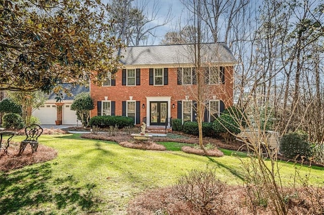 colonial house featuring a garage, brick siding, a front yard, and french doors