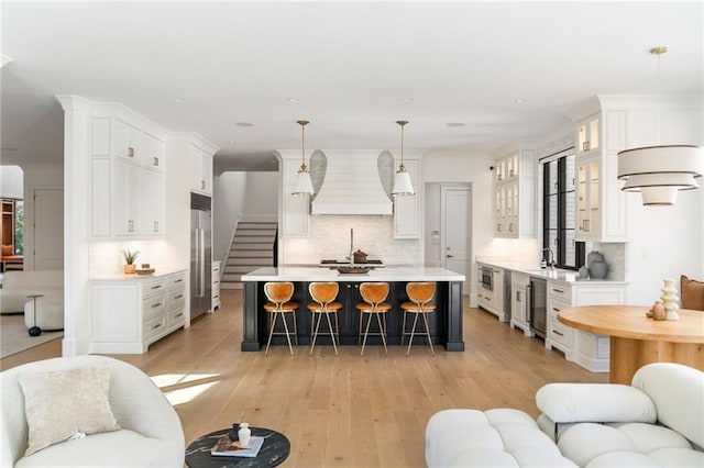 kitchen with a breakfast bar area, open floor plan, stainless steel built in refrigerator, light countertops, and premium range hood