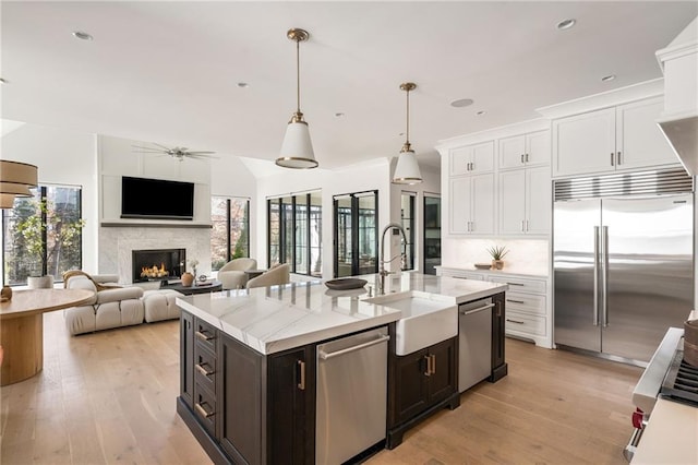 kitchen featuring stainless steel appliances, a healthy amount of sunlight, white cabinets, a sink, and a lit fireplace