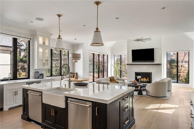 kitchen with a warm lit fireplace, white cabinets, a sink, vaulted ceiling, and stainless steel dishwasher