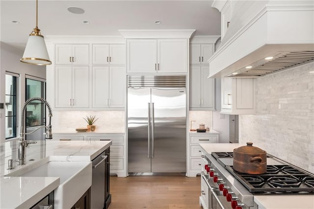 kitchen featuring premium appliances, decorative light fixtures, custom exhaust hood, white cabinetry, and a sink